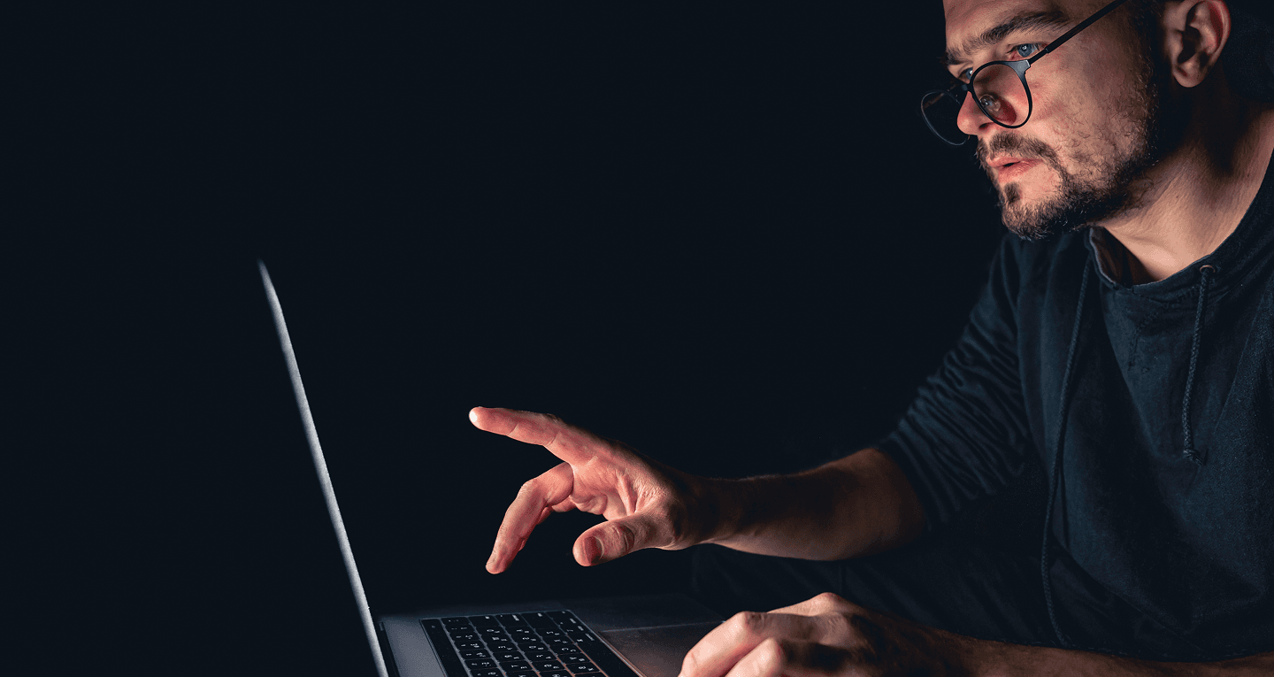 Person interacting with a laptop in a dark workspace.
